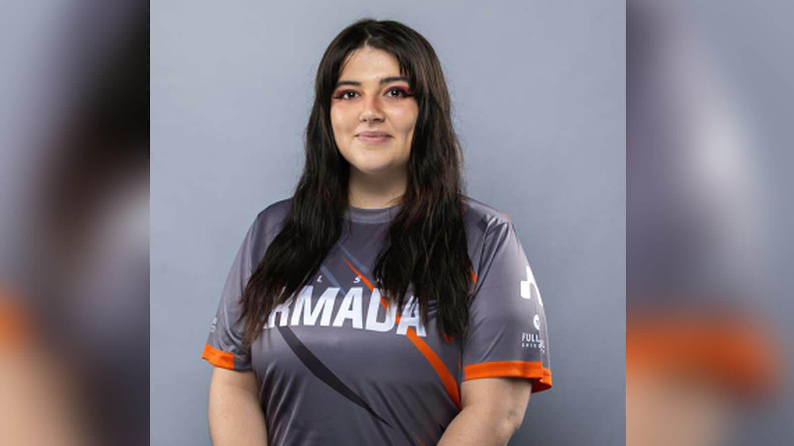 Brittanny MacCleod stands against a gray background and smiles. She has long brown hair and is wearing a gray Armada jersey.