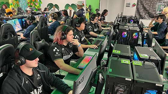 Dozens of Armada players sit in gaming chairs at desktop computers. They are wearing headphones and playing video games.